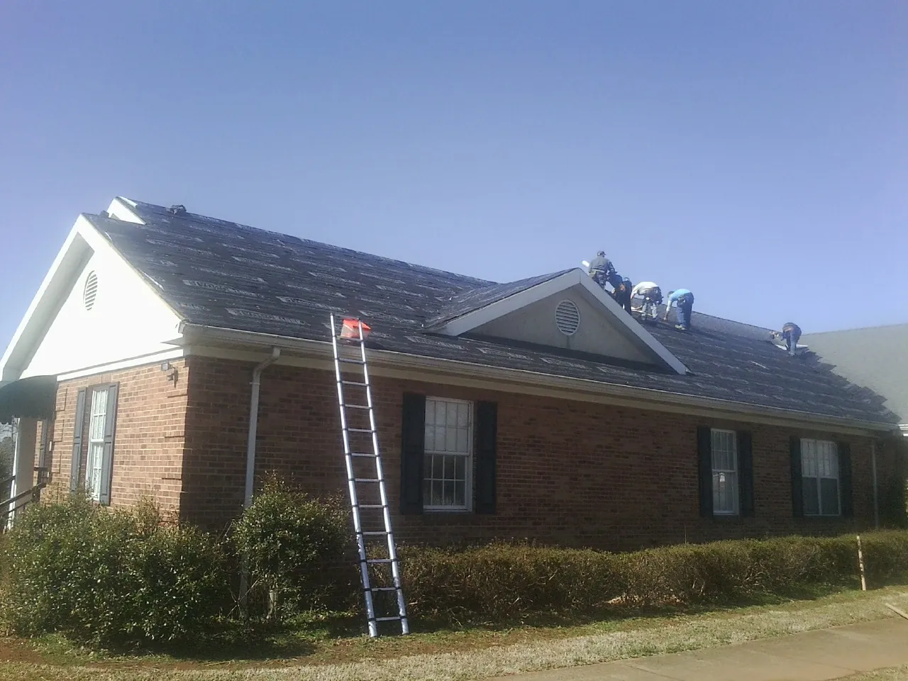 Crew tearing shingles off a brick ranch roof with a ladder set — Metal Roof Repair work by our crew in Empire