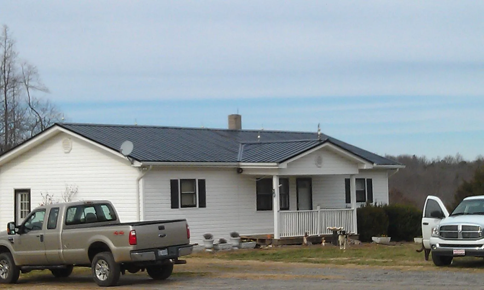 Finished dark metal roof on a white ranch home with work trucks parked in Empire